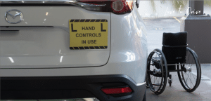 Rear view of white car with hand controls in use learner plates and wheelchair next to driver door